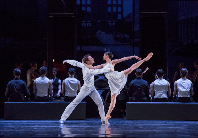 A woman on pointe in arabesque. Her arm hooks around her partners head and he steadies her by holding her rib cage.